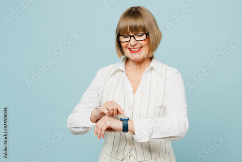 Blonde successful employee business woman 50s wear white classic suit glasses formal clothes look at smart watch check time isolated on plain pastel light blue background. Achievement career concept.