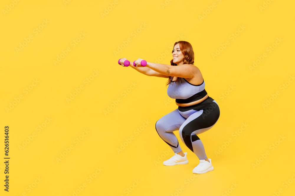 Full body side view young chubby plus size big fat fit woman wear blue top warm up training hold dumbbells do squat lunges isolated on plain yellow background studio home gym. Workout sport concept. Full body side view young chubby plus size big fat fit woman wear blue top warm up training hold dumbbells do squat lunges isolated on plain yellow background studio home gym. Workout sport concept.