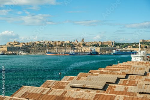 Roofs of warehouses in foreground, cargo ship in front of historic old town of Valletta