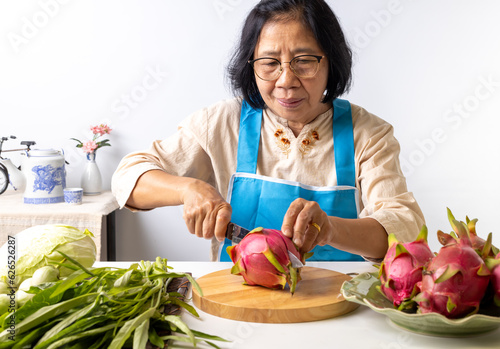 Asian senior woman slicing dragon fruit in the kitchen