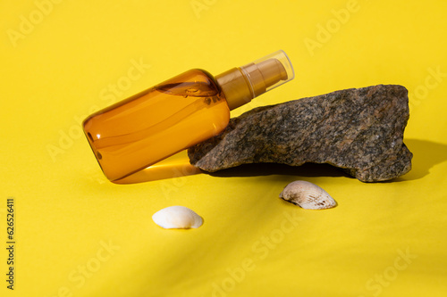 Unbranded cosmetic mockup bottle of sunscreen soothing body oil displayed on a small rock near sea shells. UV protection photo