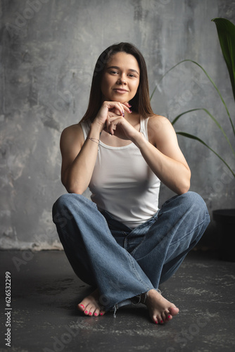 Portrait of a young attractive girl in a white T-shirt and jeans. A girl of oriental appearance in the interior of a stylish apartment. Lifestyle