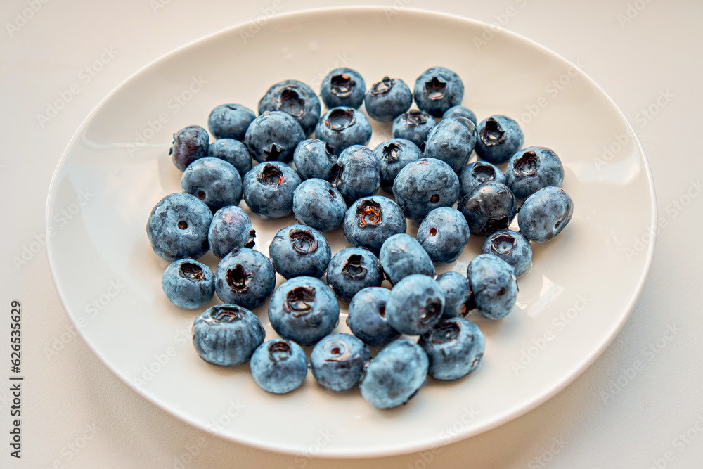 Fresh blueberries lie on a white plate on a dark background. Berries, healthy food. Selective focus. View from above. Fresh blueberries lie on a white plate on a dark background. Berries, healthy food. Selective focus. View from above.