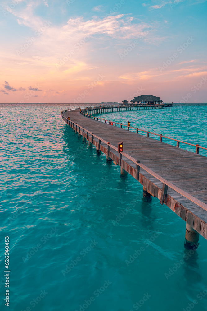 Sunset on Maldives island, luxury water villas resort, wooden pier. Beautiful colorful sky clouds and beach coast seascape background. Summer vacation landscape, Exotic tourism destination banner