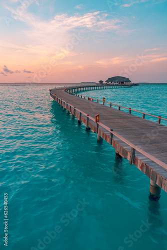 Sunset on Maldives island, luxury water villas resort, wooden pier. Beautiful colorful sky clouds and beach coast seascape background. Summer vacation landscape, Exotic tourism destination banner