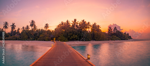 Sunset on Maldives island, luxury water villas resort, wooden pier. Beautiful sky clouds and beach coast background. Summer vacation landscape, palm trees silhouette led lights. Amazing destination