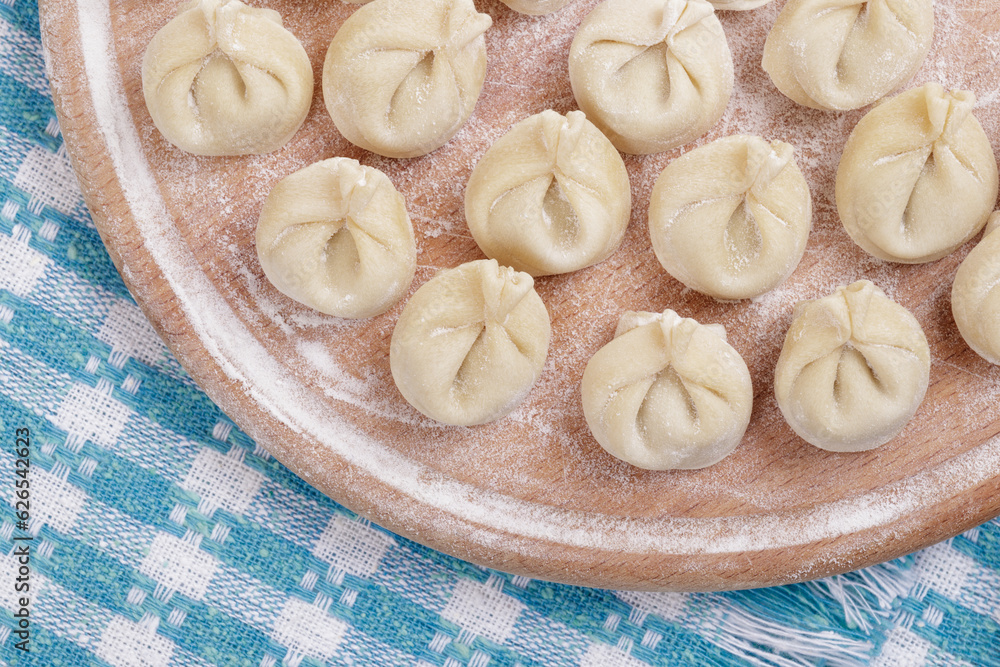 Homemade uncooked dumplings on a wooden board on the checkered tablecloth. Dumplings closeup. Top view Homemade uncooked dumplings on a wooden board on the checkered tablecloth. Dumplings closeup. Top view