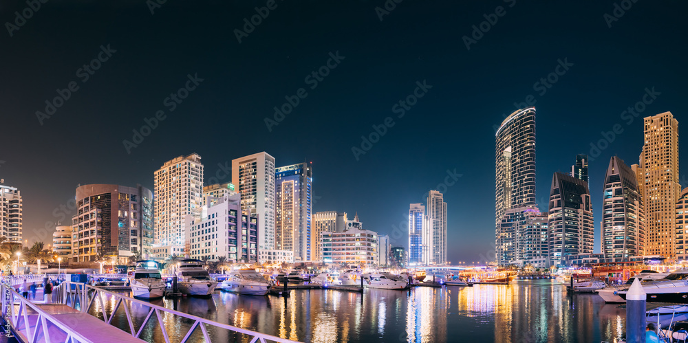 Dubai Marina Port, UAE, United Arab Emirates - Beautiful Night View Of Dubai Marina Towers. Yachts Moored Near City Pier, Jetty In Evening Night Illuminations. Panorama, Panoramic View.