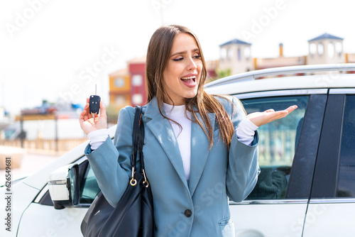 Foto Young pretty woman holding car keys at outdoors with surprise facial expression