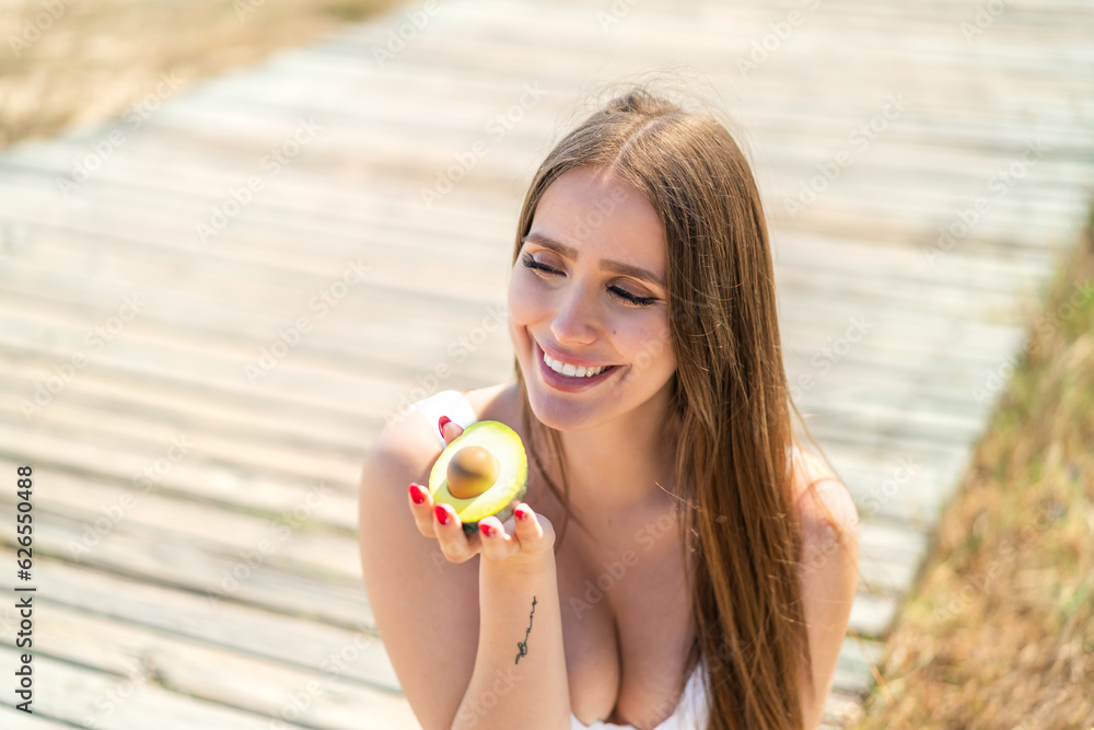 Young woman at outdoors holding an avocado with happy expression Young woman at outdoors holding an avocado with happy expression