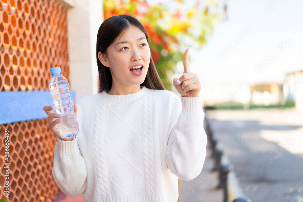 Pretty Chinese woman with a bottle of water at outdoors intending to realizes the solution while lifting a finger up Pretty Chinese woman with a bottle of water at outdoors intending to realizes the solution while lifting a finger up