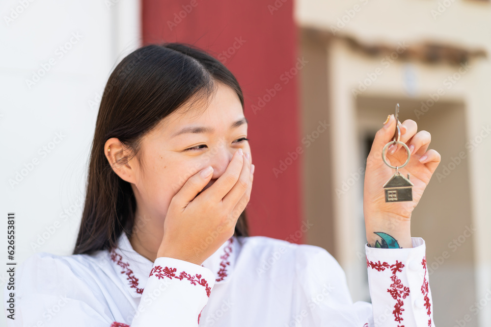Young Chinese woman at outdoors holding home keys Young Chinese woman at outdoors holding home keys