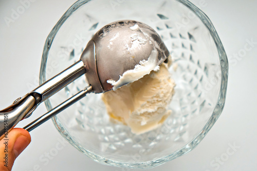A human hand puts a scoop of ice cream into a glass bowl with a scoop. Close-up