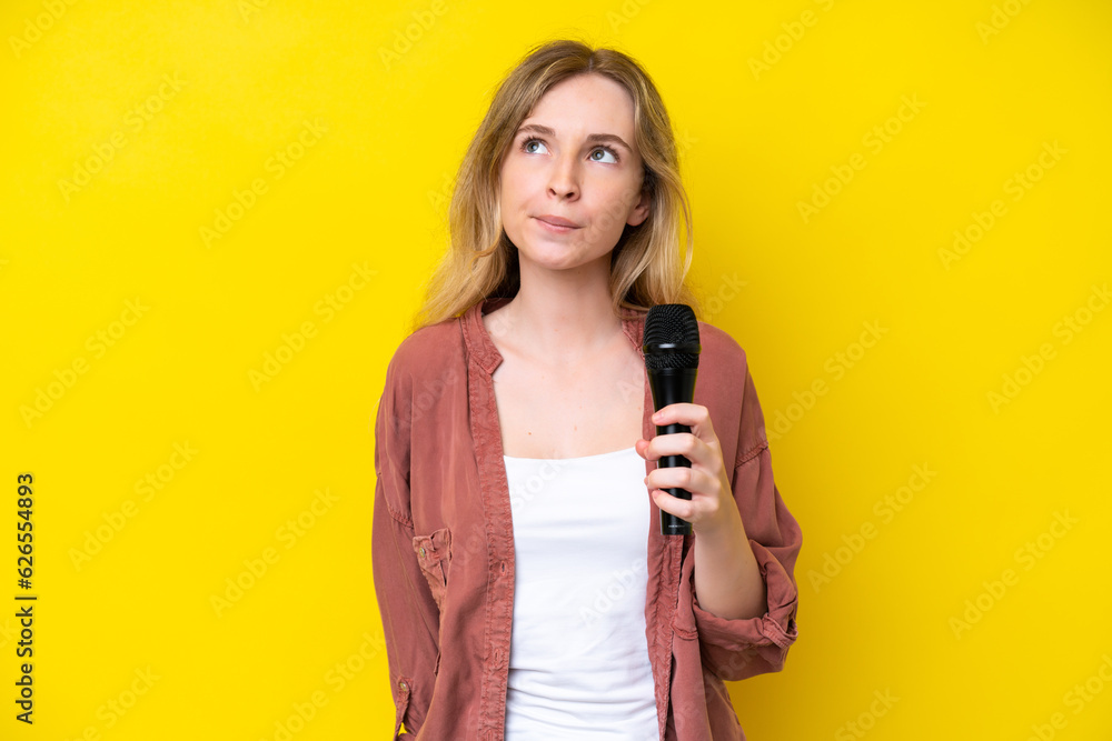 Young singer caucasian woman picking up a microphone isolated on yellow background and looking up Young singer caucasian woman picking up a microphone isolated on yellow background and looking up