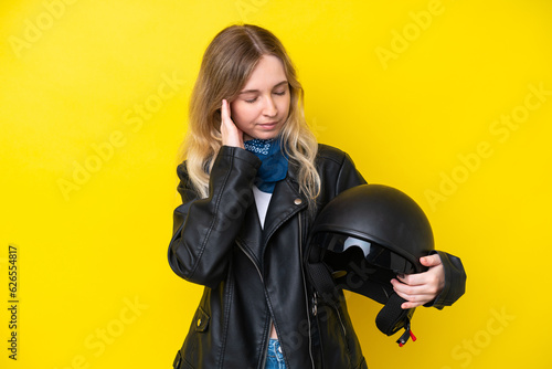 Blonde English young girl with a motorcycle helmet isolated on yellow background with headache