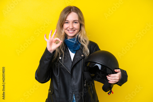 Blonde English young girl with a motorcycle helmet isolated on yellow background showing ok sign with fingers