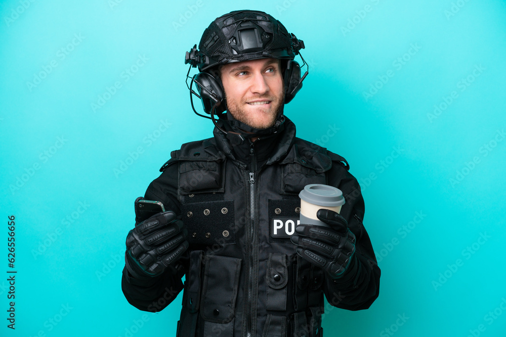SWAT caucasian man isolated on blue background holding coffee to take away and a mobile while thinking something SWAT caucasian man isolated on blue background holding coffee to take away and a mobile while thinking something