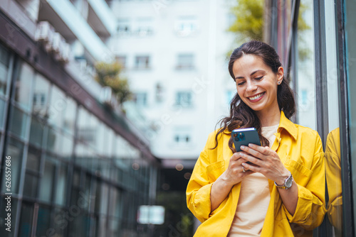 Fotografie A mixed-race businesswoman reading something funny on her mobile phone on the street while going back home from work