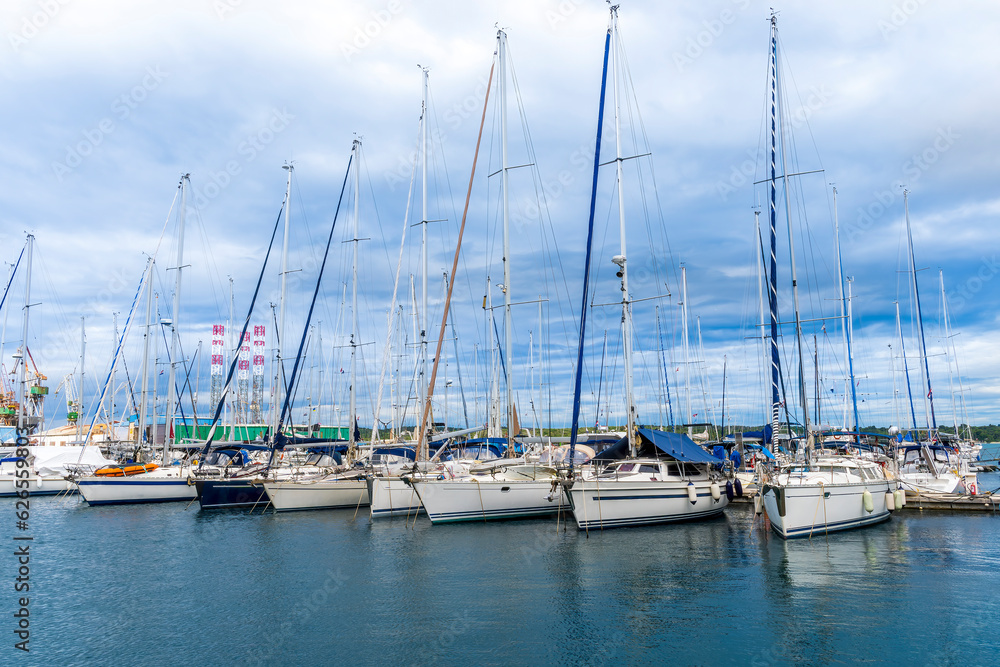 boats and yachts on pier in marine city port with masts and bulidings and blue sky on background , water cityscape of urban port