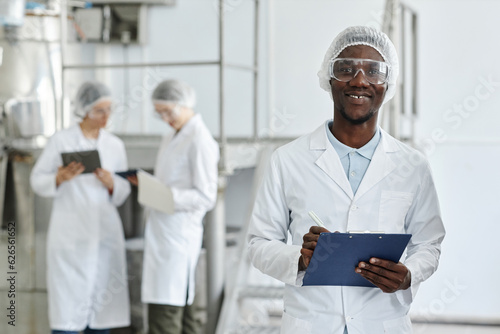 Foto Waist up portrait of black young man wearing lab coat and smiling at camera in c
