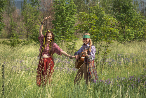 Couple of young people in hippie style. The girl is dancing, the guy is playing the guitar in a forest clearing on a sunny day