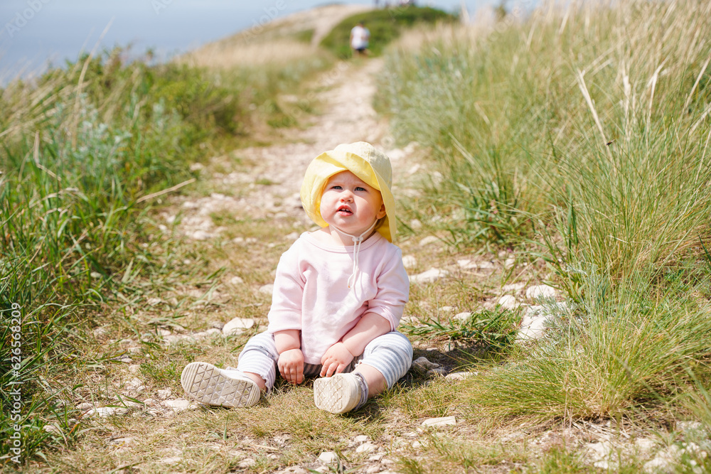 Cute baby toddler in a panama hat is sitting on the path, active childhood in the fresh air Cute baby toddler in a panama hat is sitting on the path, active childhood in the fresh air