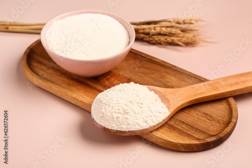 Bowl and spoon with flour on pink background, closeup