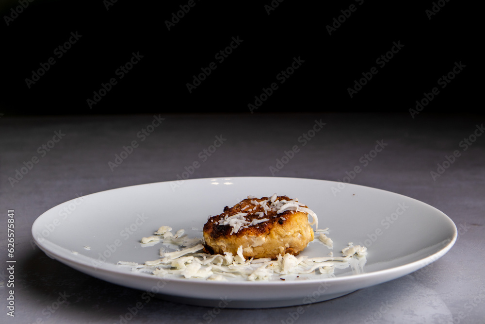 fried cutlet sprinkled with cheese lies on a plate on a black background, isolated fried cutlet sprinkled with cheese lies on a plate on a black background, isolated