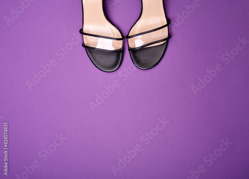 A shot capturing the toes of the summer shoes with clear vamps with black trimming and black-beige insoles. Purple background with copy space. Fashion blog or magazine concept.