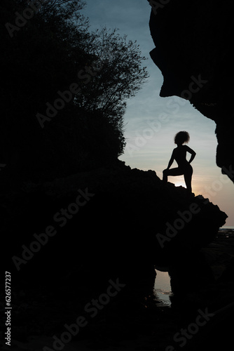The contour of a beautiful girl against the backdrop of a tropical sunset among the rocks