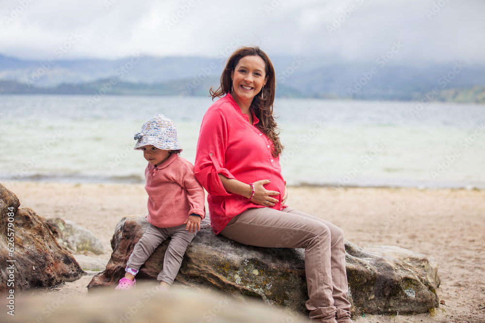 Young pregnant woman having fun with her baby girl at the beautiful white beach of Lake Tota located in the department of Boyaca at 3,015 meters above sea level in Colombia