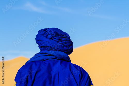 Close-up. Background. Berber in blue traditional clothing against the backdrop of a large dune. View from behind. Tunisia, Africa