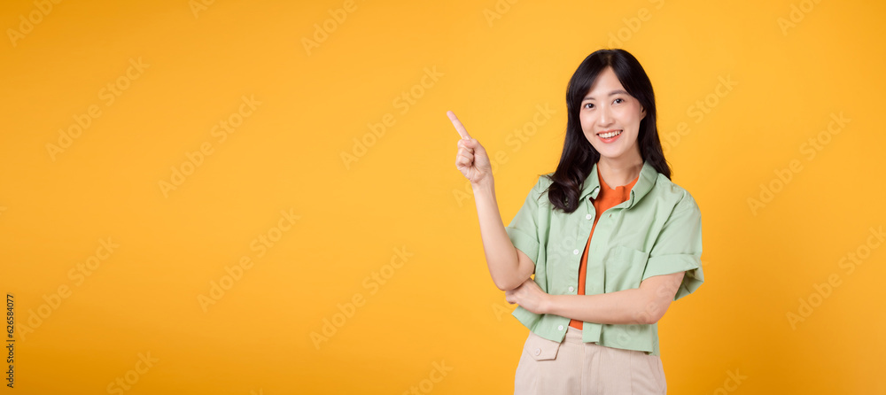 young 30s Asian woman wearing a green shirt on an orange shirt, pointing with excitement to free copy space. Discover the concept of discount shopping promotion with captivating image. young 30s Asian woman wearing a green shirt on an orange shirt, pointing with excitement to free copy space. Discover the concept of discount shopping promotion with captivating image.