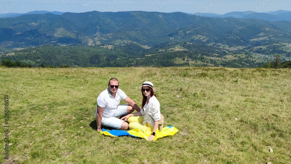 A couple of tourists are resting, sitting in the Carpathians, enjoying the scenery. Summer vacation. couple in love with ukraine flag A couple of tourists are resting, sitting in the Carpathians, enjoying the scenery. Summer vacation. couple in love with ukraine flag