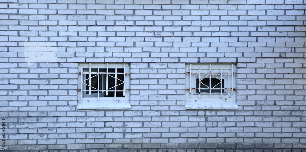 Two small barred windows in a white brick wall Two small barred windows in a white brick wall