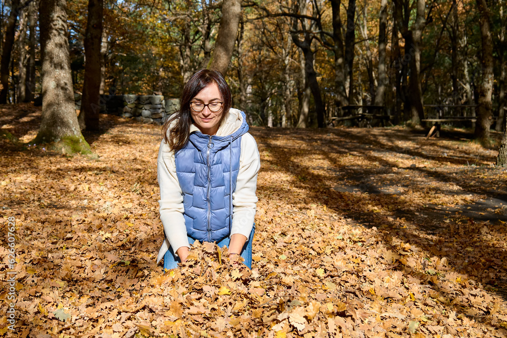 Happy middle-aged woman throwing the fallen leaves up in autumn forest. Spending time in fall nature for wellness and healthy lifestyle. Freedom and unity with nature concept. Happy middle-aged woman throwing the fallen leaves up in autumn forest. Spending time in fall nature for wellness and healthy lifestyle. Freedom and unity with nature concept.