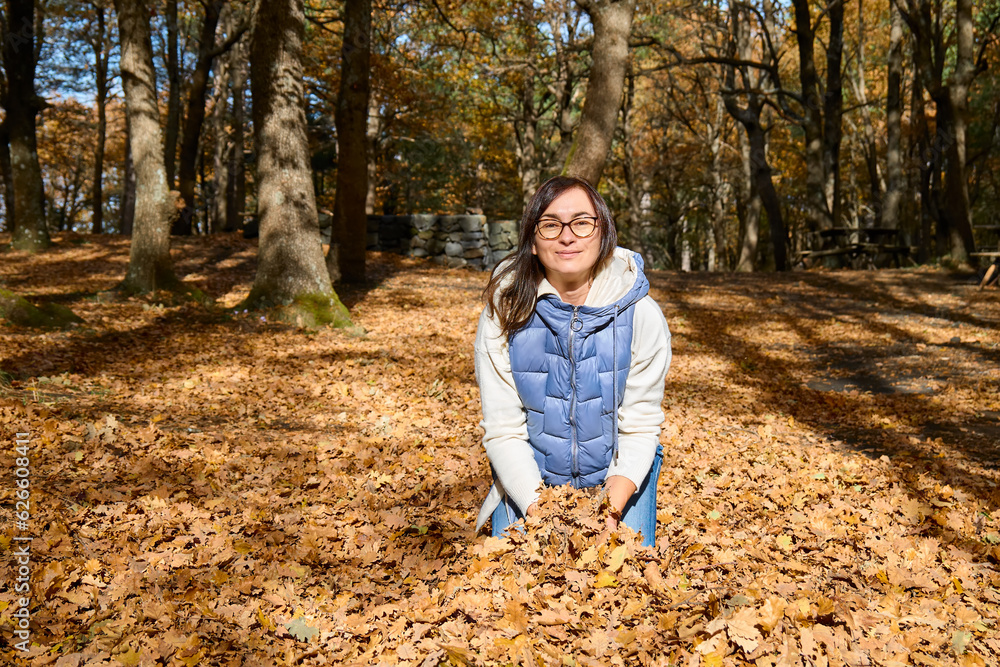Happy middle-aged woman throwing the fallen leaves up in autumn forest. Spending time in fall nature for wellness and healthy lifestyle. Freedom and unity with nature concept. Happy middle-aged woman throwing the fallen leaves up in autumn forest. Spending time in fall nature for wellness and healthy lifestyle. Freedom and unity with nature concept.