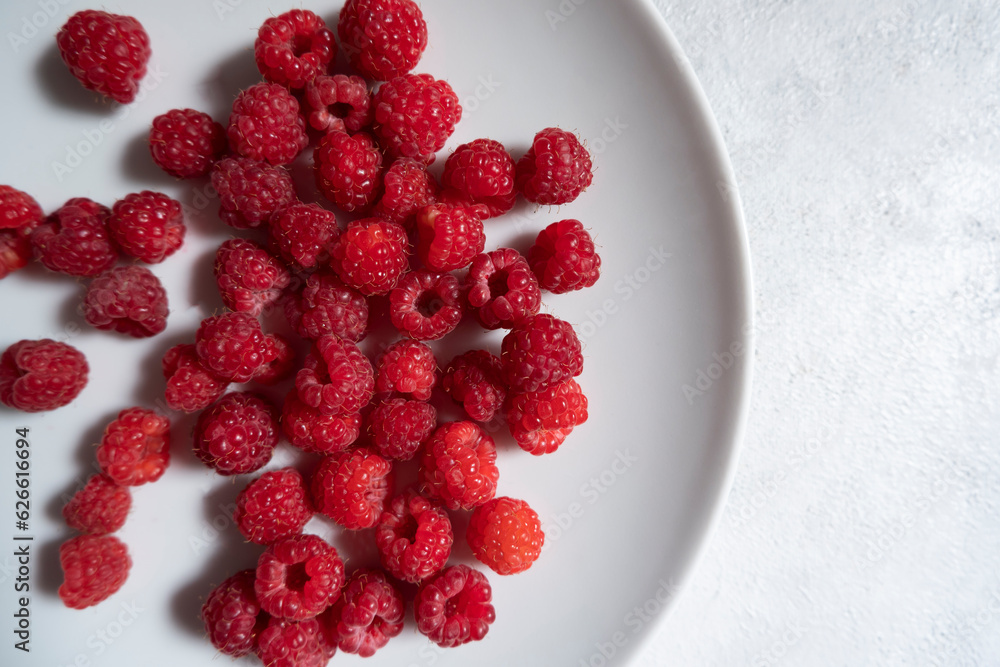 Fresh, ripe raspberries in a light plate on a light background. Photo from above. The concept of proper nutrition, diet Fresh, ripe raspberries in a light plate on a light background. Photo from above. The concept of proper nutrition, diet