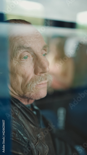 Close up of pensive senior looks out window while traveling in train compartment, view through glass