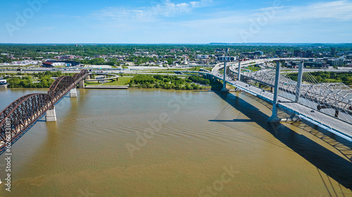 Three truss suspension bridges crossing Ohio River water aerial toward city distant green shore
