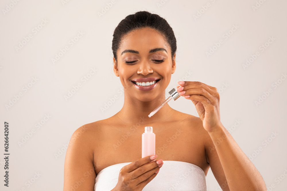 Smiling attractive young black woman applying face serum Smiling attractive young black woman applying face serum