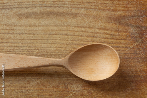 New wooden spoon on light brown textured wooden background. The surface of the scratched cutting board, top view. Food background