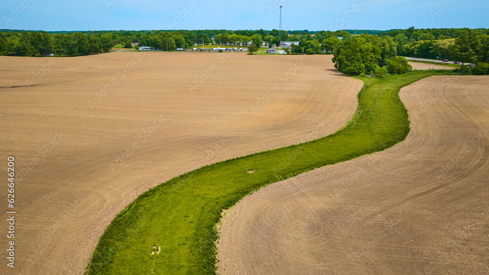 Aerial snaking green patch of land surrounded by barren dirt farmland
