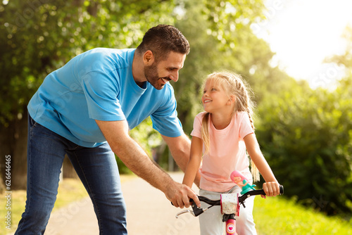 A father's guide. Girl learning to ride a bicycle with her father in the park, having fun together on weekend