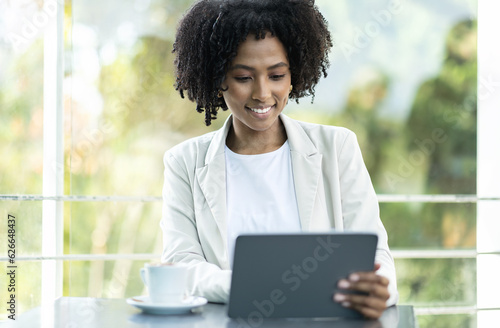 Cheerful young black lady entrepreneur sitting at cafe, using tablet
