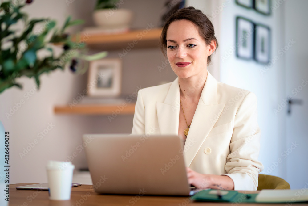 Confident young woman sitting at table and using laptop for work at home Confident young woman sitting at table and using laptop for work at home