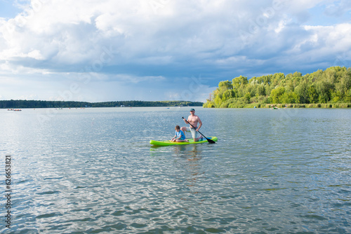 father and son ride a SUP board, father and child spend time outdoors on the lake