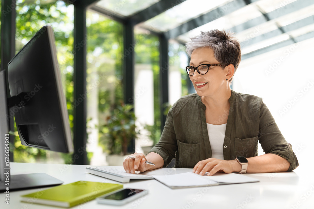 Attractive middle aged woman working on pc at green office Attractive middle aged woman working on pc at green office