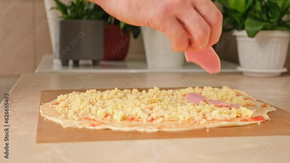 A man sprinkles mozzarella cheese on a layer of yeast dough, the basis for pizza. Cooking homemade pizza. A man sprinkles mozzarella cheese on a layer of yeast dough, the basis for pizza. Cooking homemade pizza.