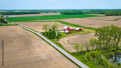 Aerial red farmhouse with barn, shed, lake side property small forest landscaping empty fields asset photo